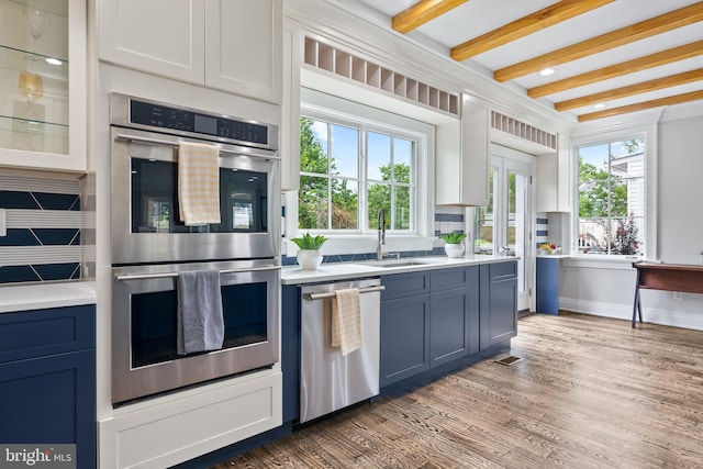 kitchen featuring beam ceiling, stainless steel appliances, light countertops, a sink, and wood finished floors