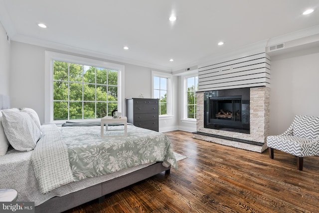 bedroom featuring a glass covered fireplace, ornamental molding, wood finished floors, and visible vents