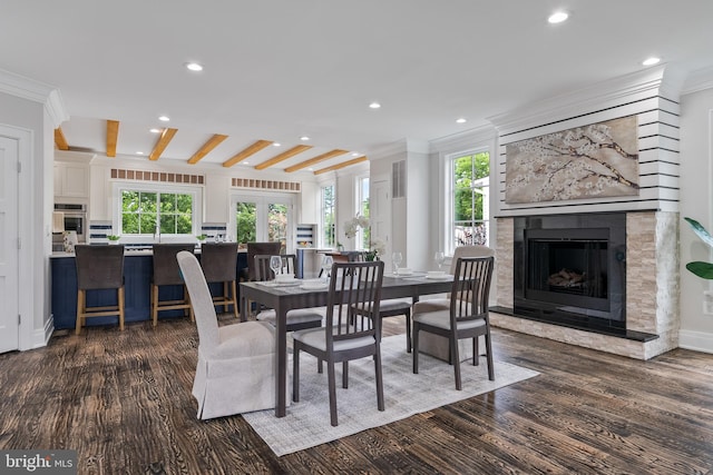 dining area with a healthy amount of sunlight, dark wood finished floors, a fireplace with raised hearth, and crown molding