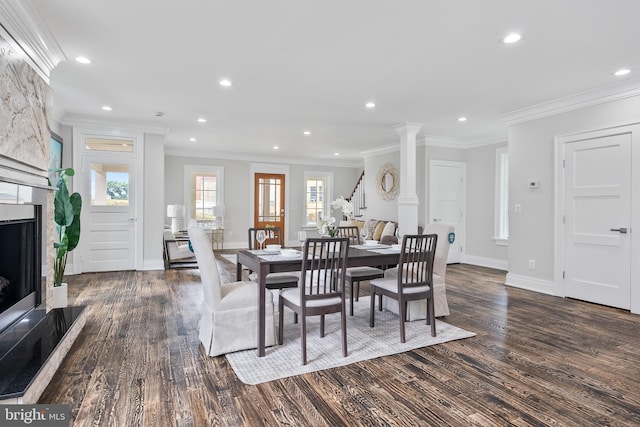 dining area with a large fireplace, crown molding, decorative columns, and dark wood-style flooring