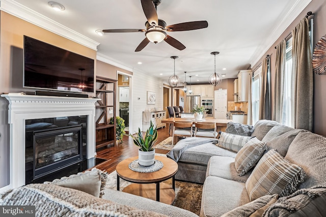 living area featuring a fireplace with flush hearth, ornamental molding, recessed lighting, wood finished floors, and a ceiling fan