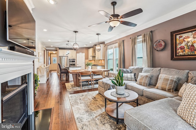 living area featuring a ceiling fan, dark wood-style floors, a fireplace, recessed lighting, and ornamental molding