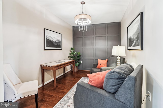 sitting room featuring dark wood-style floors, a decorative wall, baseboards, and a notable chandelier