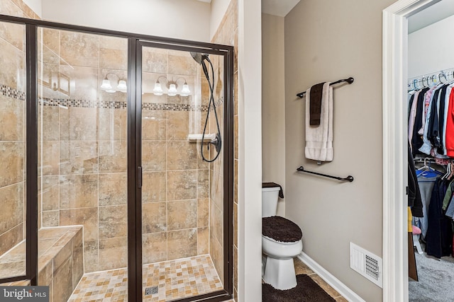 bathroom featuring visible vents, a walk in closet, baseboards, toilet, and a stall shower