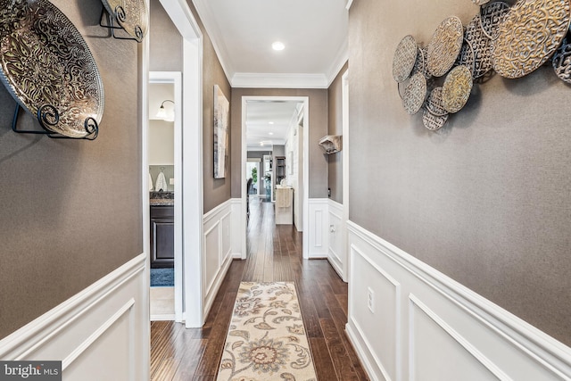 hallway with wainscoting, ornamental molding, dark wood-style flooring, and a decorative wall