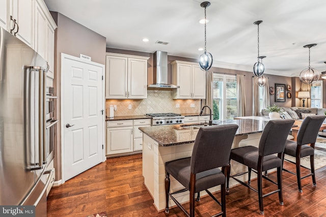 kitchen with a sink, decorative backsplash, stainless steel fridge, wall chimney exhaust hood, and dark wood-style flooring