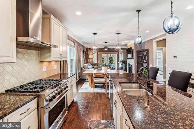 kitchen featuring wall chimney range hood, dark wood finished floors, open floor plan, high end stainless steel range oven, and a sink