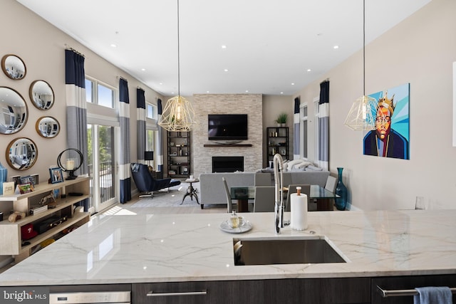 kitchen featuring light stone counters, a fireplace, a sink, pendant lighting, and open floor plan