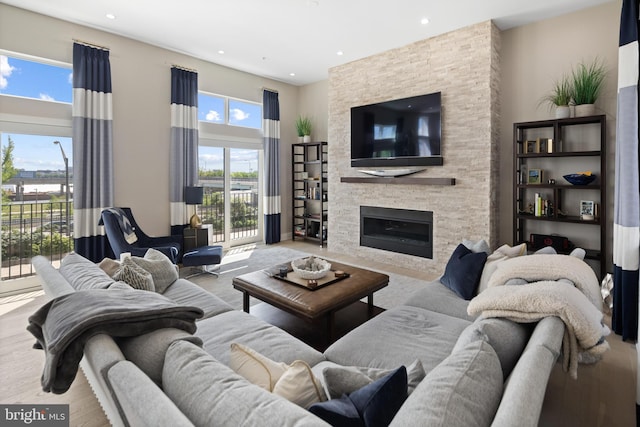 living area featuring recessed lighting, a stone fireplace, wood finished floors, and a towering ceiling