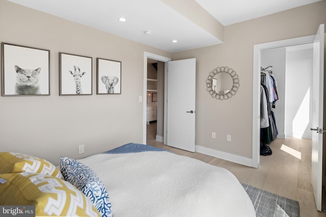 bedroom with a spacious closet, baseboards, recessed lighting, wood finished floors, and a closet