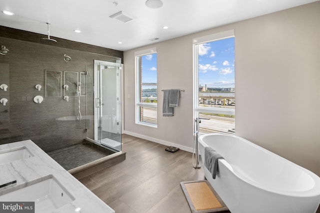 full bath with baseboards, a soaking tub, double vanity, a stall shower, and a sink