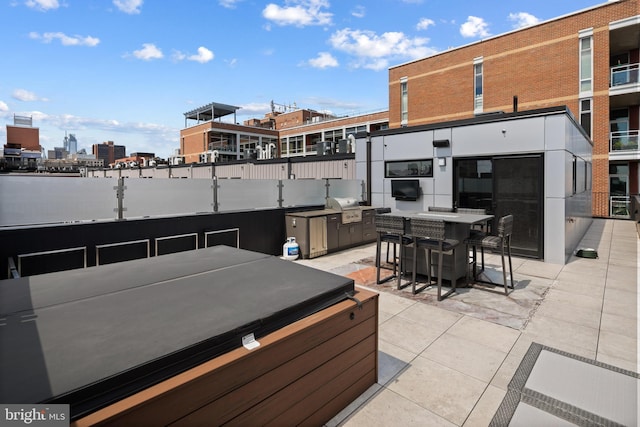 view of patio / terrace with grilling area, a hot tub, a city view, outdoor dining space, and an outdoor kitchen