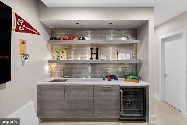 bar featuring light wood finished floors, backsplash, beverage cooler, indoor wet bar, and a sink