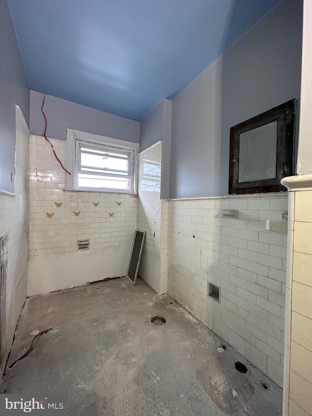 bathroom featuring unfinished concrete floors, tile walls, and wainscoting