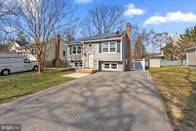 split foyer home featuring a front lawn, a gate, roof mounted solar panels, fence, and a chimney