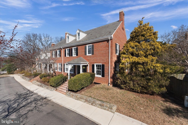 view of front of property featuring a chimney, fence, and brick siding