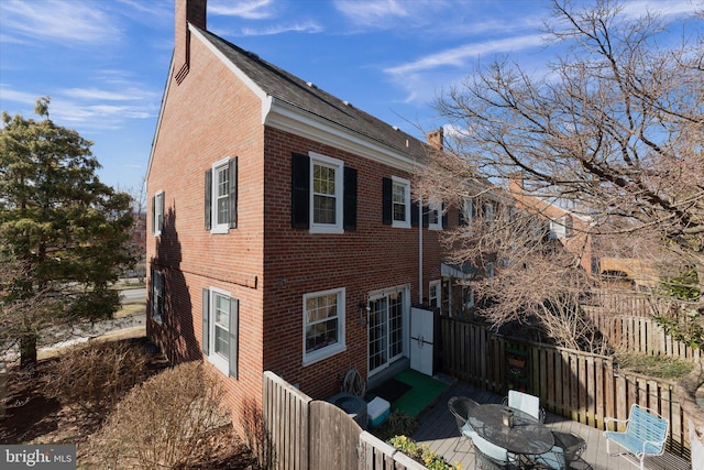 view of side of home featuring brick siding, a chimney, and fence