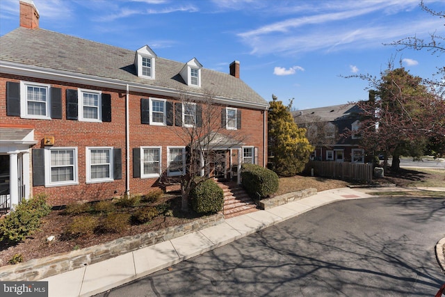 view of front of home with brick siding, fence, and a chimney