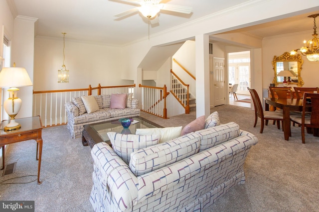 carpeted living area with visible vents, ceiling fan with notable chandelier, stairs, and crown molding