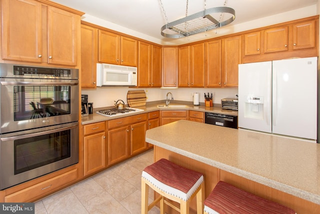 kitchen featuring white appliances, light tile patterned floors, a sink, light countertops, and a kitchen bar