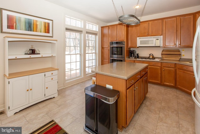 kitchen featuring white microwave, a kitchen island, brown cabinets, stainless steel double oven, and gas cooktop