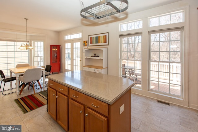 kitchen with visible vents, a kitchen island, hanging light fixtures, french doors, and brown cabinets