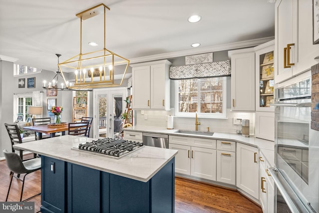 kitchen featuring stainless steel appliances, a kitchen island, a sink, white cabinets, and an inviting chandelier