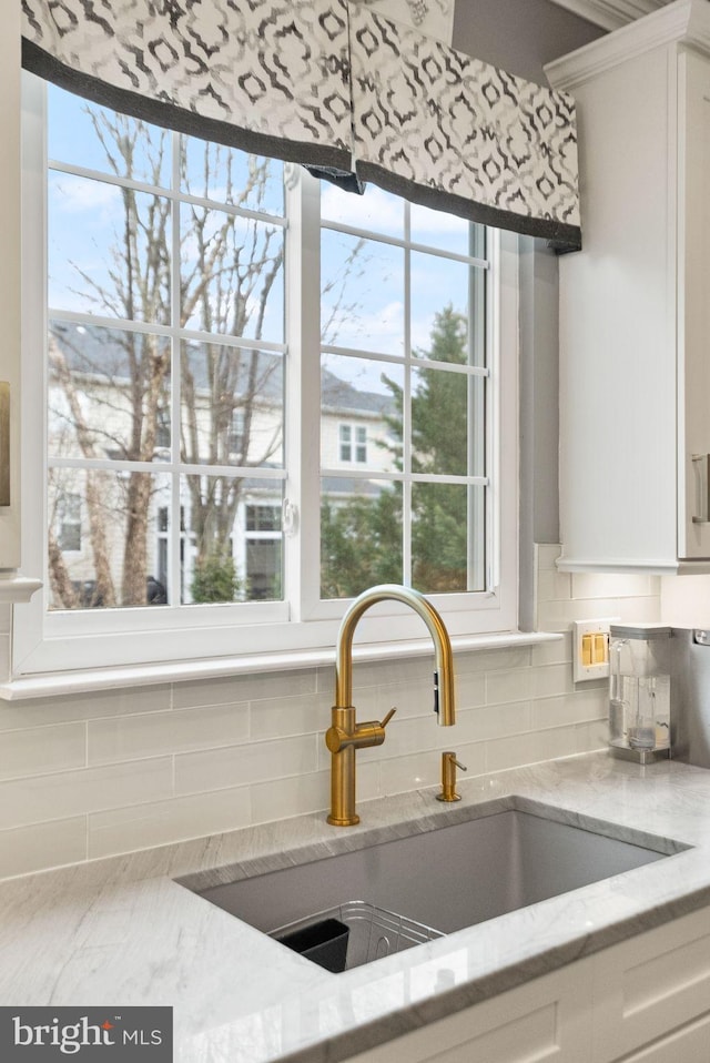 room details featuring white cabinetry, a sink, backsplash, and light stone countertops