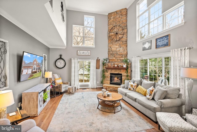 living room featuring a fireplace, crown molding, light wood-style flooring, and a towering ceiling