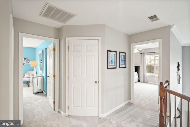 corridor with an upstairs landing, visible vents, and light colored carpet