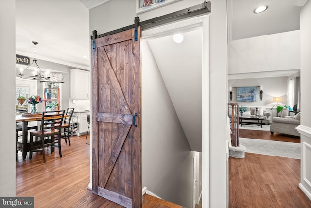 corridor with a barn door, wood finished floors, crown molding, a chandelier, and recessed lighting