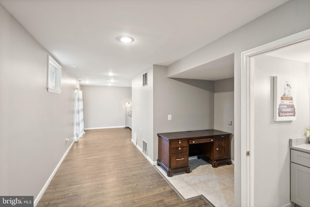 corridor with light wood-type flooring, visible vents, and baseboards