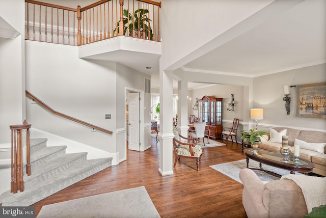 living room with crown molding, a towering ceiling, wood finished floors, baseboards, and stairs