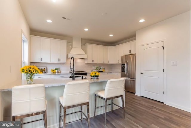 kitchen with dark wood-style flooring, white cabinets, custom exhaust hood, backsplash, and stainless steel fridge