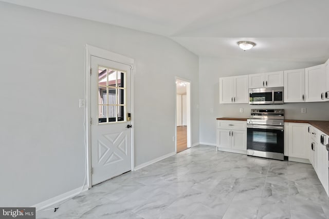 kitchen with dark countertops, marble finish floor, stainless steel appliances, white cabinets, and lofted ceiling