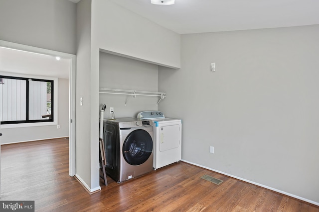 clothes washing area featuring washing machine and clothes dryer, baseboards, wood finished floors, and visible vents