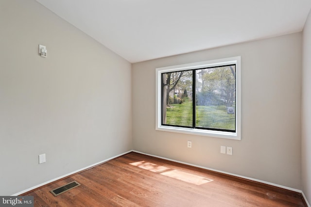 empty room featuring vaulted ceiling, baseboards, wood finished floors, and visible vents