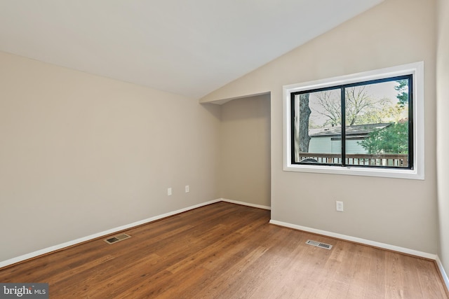 spare room with vaulted ceiling, visible vents, baseboards, and wood finished floors
