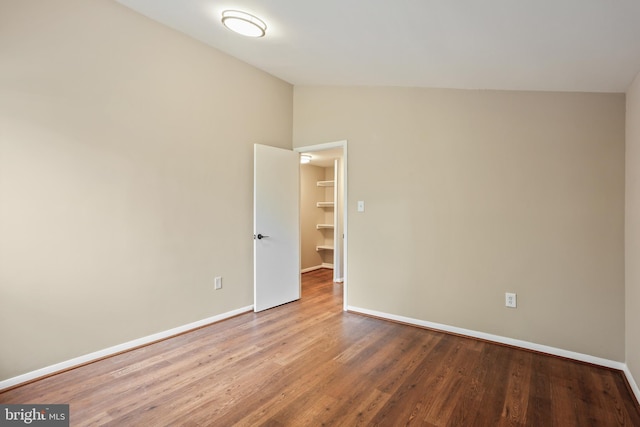 empty room with wood finished floors, baseboards, and vaulted ceiling