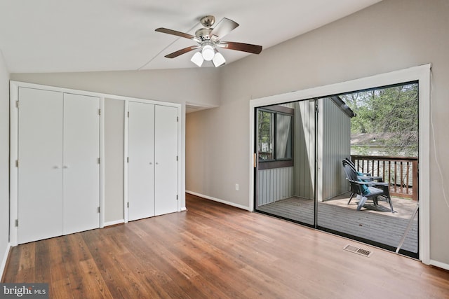 unfurnished bedroom with lofted ceiling, multiple closets, wood finished floors, visible vents, and access to outside