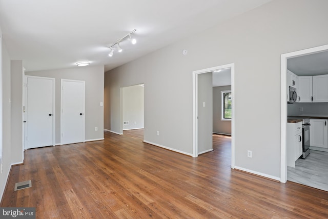 unfurnished living room with vaulted ceiling, wood finished floors, visible vents, and baseboards