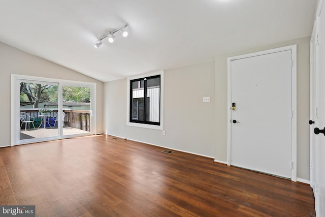 spare room featuring dark wood finished floors, vaulted ceiling, and visible vents