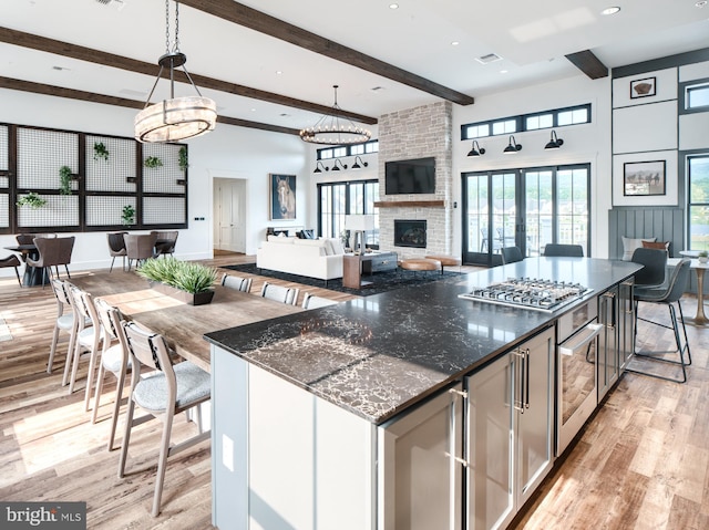 kitchen with wine cooler, a large fireplace, light wood finished floors, beamed ceiling, and stainless steel gas stovetop