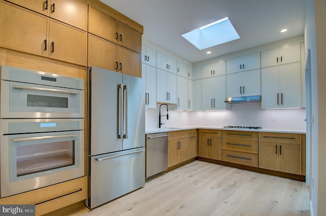 kitchen with tasteful backsplash, stainless steel appliances, light countertops, under cabinet range hood, and a sink