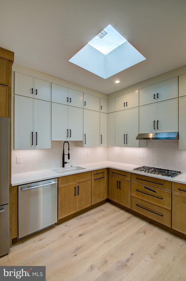 kitchen featuring light wood-style floors, appliances with stainless steel finishes, decorative backsplash, and a sink