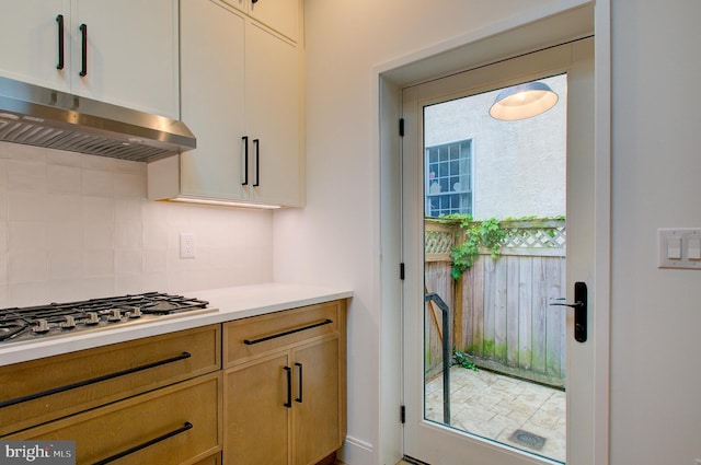 kitchen with plenty of natural light, decorative backsplash, light countertops, under cabinet range hood, and stainless steel gas stovetop