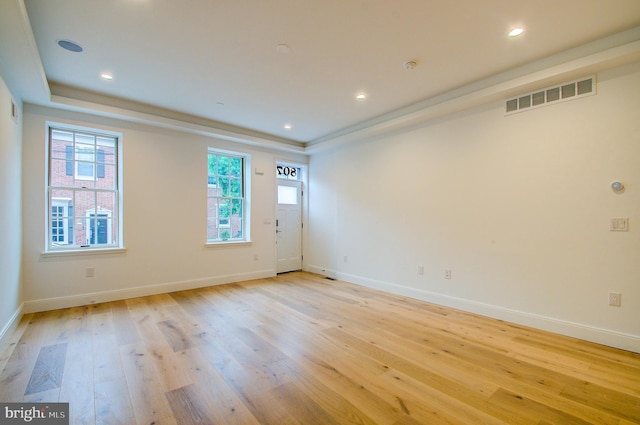 spare room featuring a tray ceiling, light wood-type flooring, visible vents, and baseboards