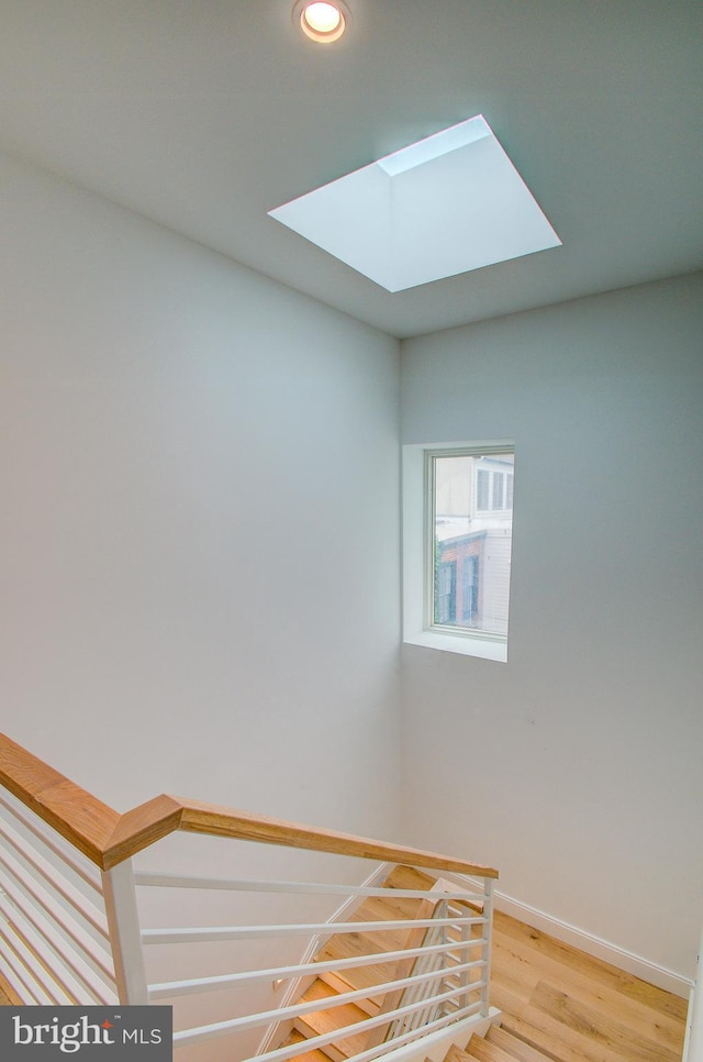 stairway featuring a skylight, baseboards, wood finished floors, and recessed lighting