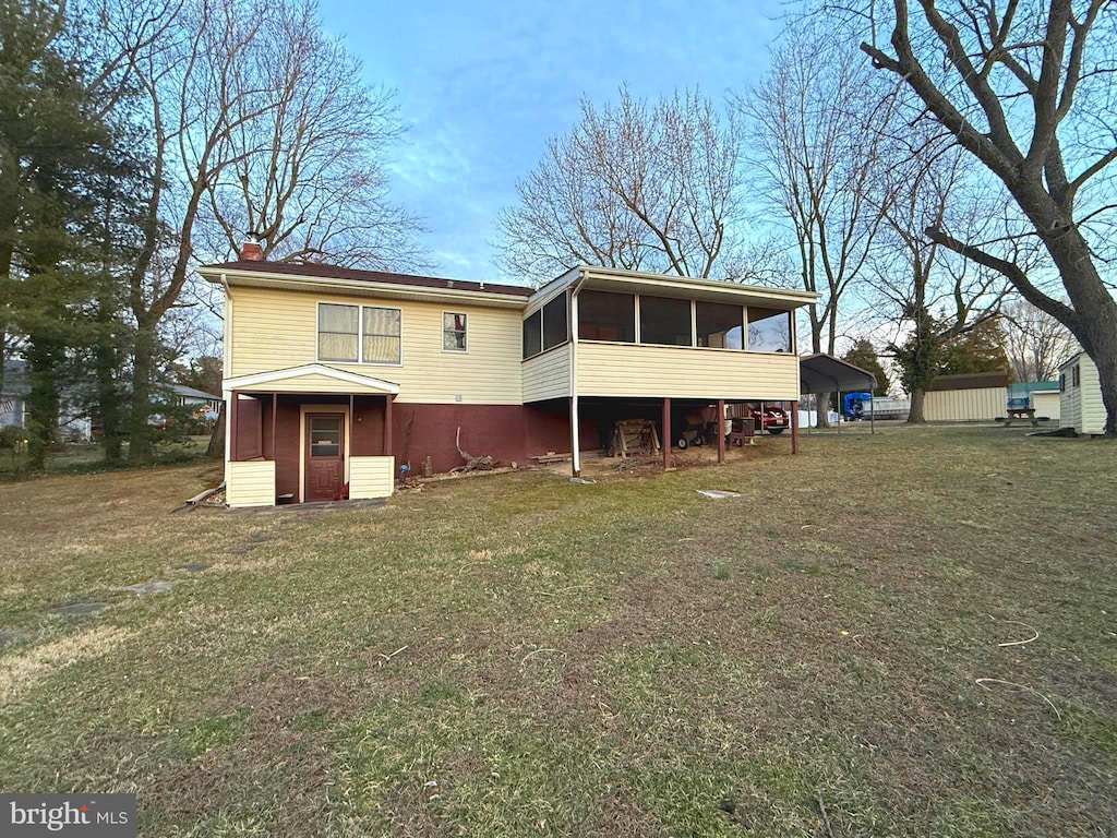 rear view of house with a carport, a sunroom, a lawn, and a chimney