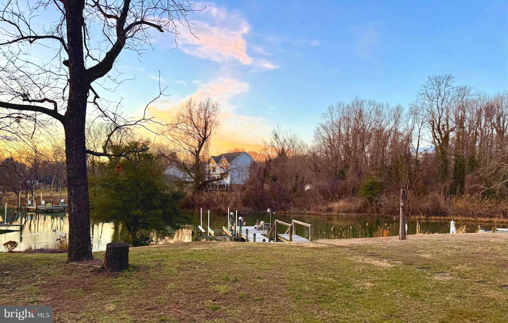 yard at dusk featuring a water view, a boat dock, and boat lift